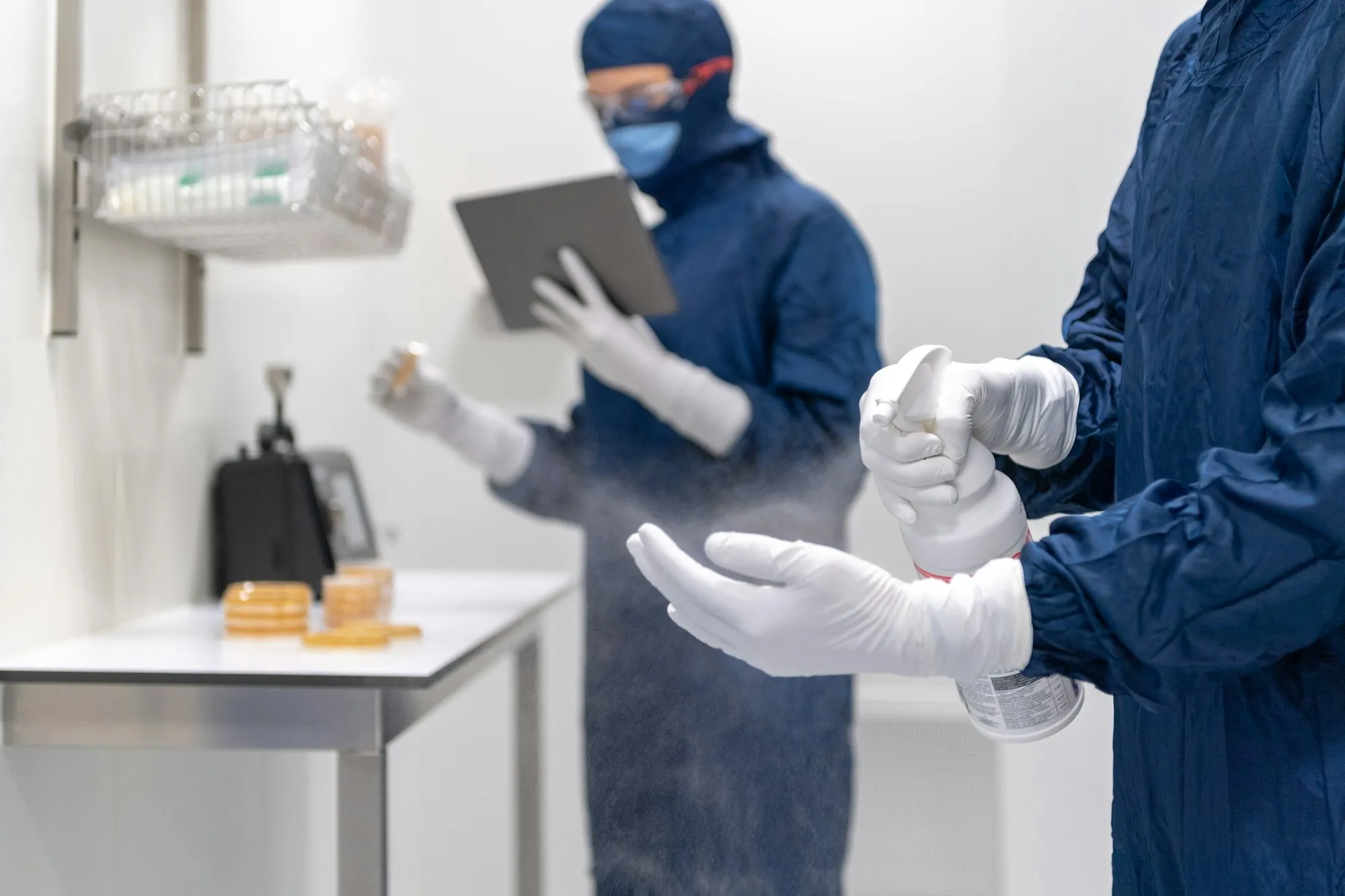 Cleanroom personnel in gowns disinfecting gloved hands